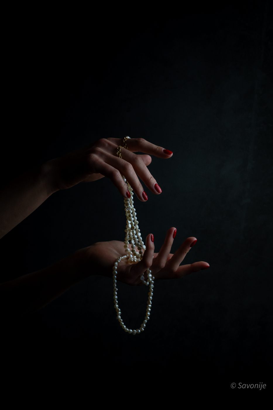Hands lifting a strand of baroque pearls out of shadow